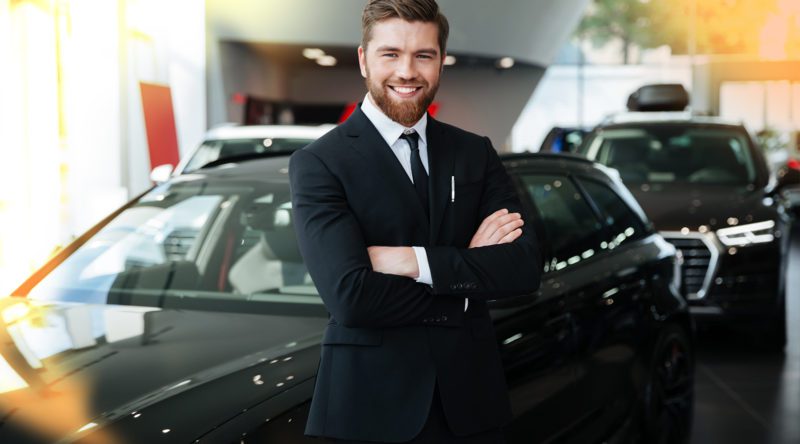 Automobilkaufmann mit stabiler Pose und verschränkten Armen und einem lächeln in einer Autohaus.