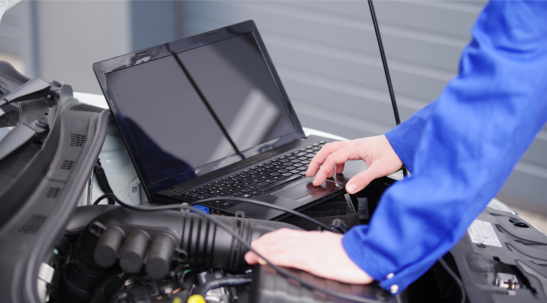 Kfz-Meister arbeiten selbst praktisch in der Werkstatt mit und misst mit seinem Laptop die Werte vom Fahrzeug ab.