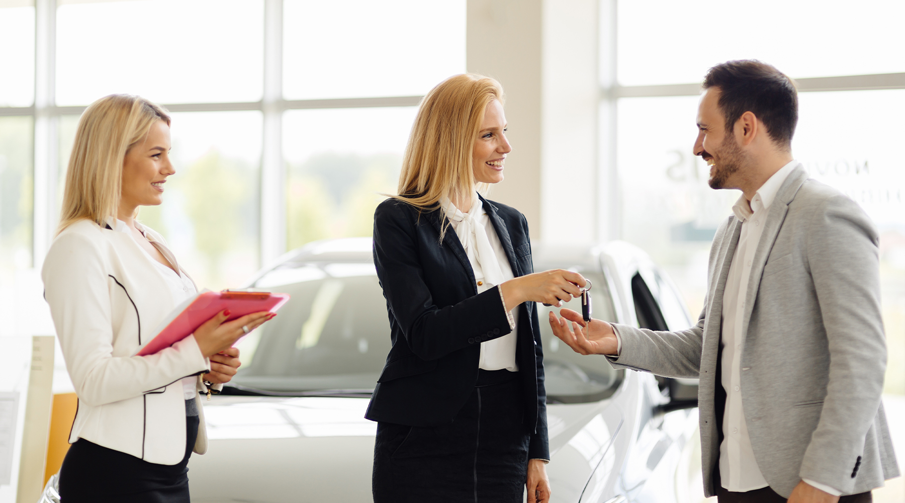 Filialleiterin im Autohaus Filialleiterin im Autohaus übergibt einem Kunde Autoschlüssel. Auch eine Service Assistentin ist zu sehen.