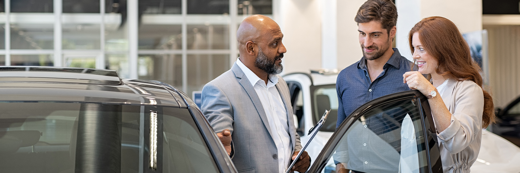 Garantiesachbearbeiter mit Kunden in der Beratung an einem Fahrzeug mit offener Fahrertür.