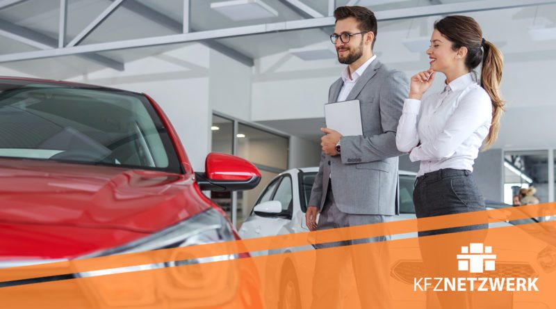 Verkaufsberater Gebrauchtwagen mit einer Kundin in einer Autogalerie vor einem Fahrzeug. KFZ Netzwerk Logo ist zu sehen.