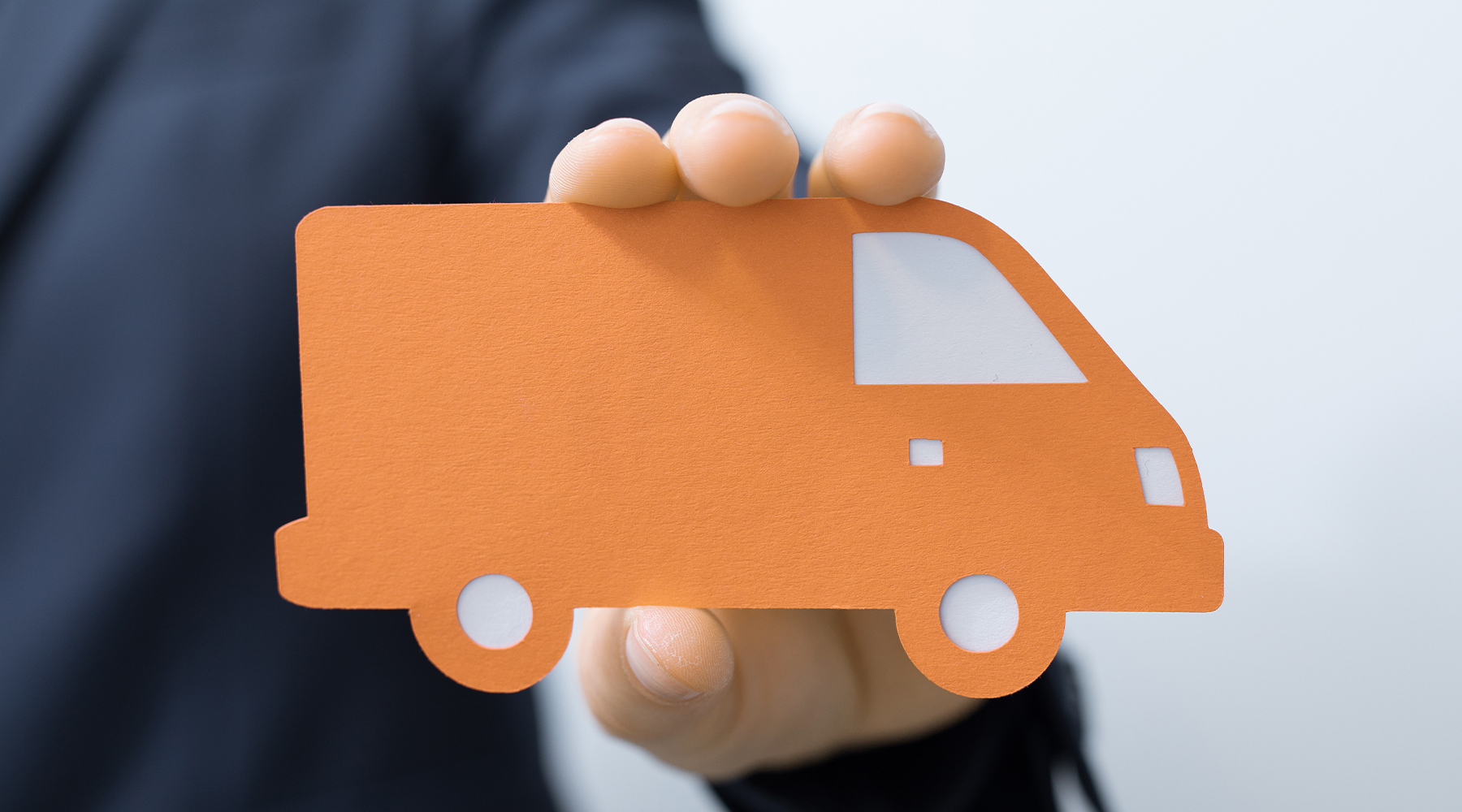 Verkaufsberater für Nutzfahrzeuge hält einen in Papier zurechtgeschnittenen Transporter in orangener Farbe in der Hand.