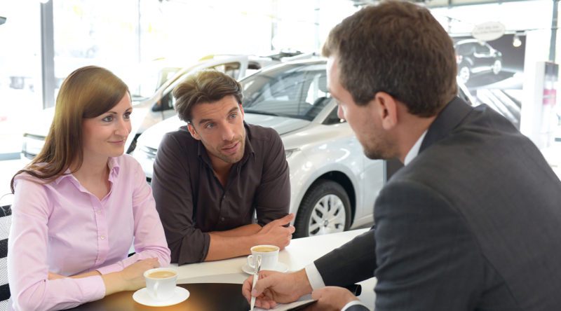 Verkaufsberater für Neuwagen beratend mit Kunden in einer Autogalerie. Kunden Trinken Kaffee